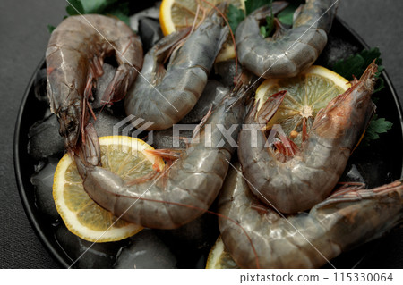 Large King prawns on lemon slices and ice. Black plate. Black background Large King prawns on lemon slices and ice. Black plate. Black background 115330064