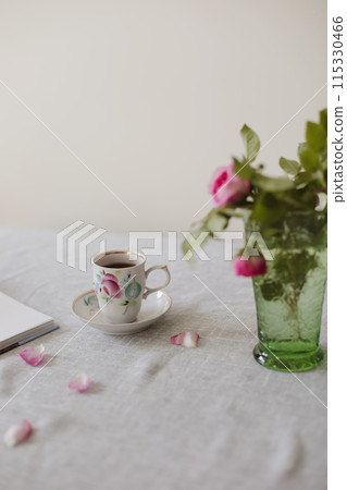 Moody summer still life. Table composition with cup of coffee, tea and beautiful floral bouquet with pink roses 115330466