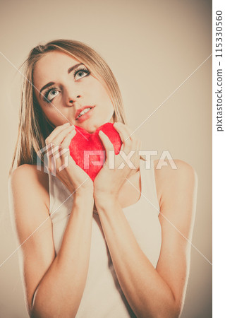Sad unhappy woman holding red heart pillow 115330560