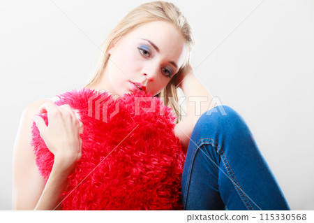 Sad unhappy woman holding red heart pillow 115330568