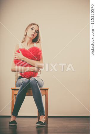 Sad unhappy woman holding red heart pillow Sad unhappy woman holding red heart pillow 115330570