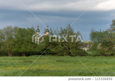 The baroque Saint-Maurice church in Ebersmunster surrounded by meadows in spring. 115330850