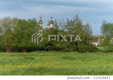 The baroque Saint-Maurice church in Ebersmunster surrounded by meadows in spring. 115330851