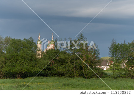 The baroque Saint-Maurice church in Ebersmunster surrounded by meadows in spring. 115330852