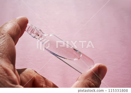 Ampoule for injection with medicines on a pink background in hand. 115331808