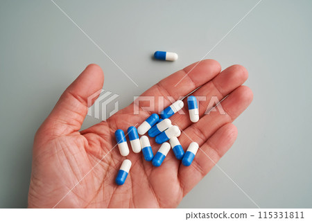 A hand holds a handful of white and blue pills on a blue background. 115331811
