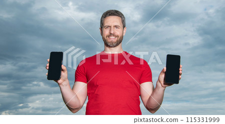 cheerful man showing phone app outdoor. man showing phone app wear red tshirt. cheerful man showing phone app outdoor. man showing phone app wear red tshirt. 115331999