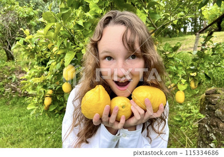 a teenage girl stands near a lemon tree and rejoices in a lemon, she sniffs them, hugs, examines a teenage girl stands near a lemon tree and rejoices in a lemon, she sniffs them, hugs, examines 115334686
