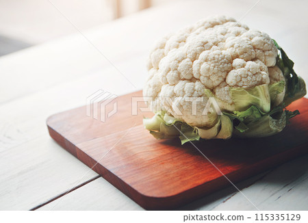 Cauliflower, wooden board and food in home for health, lunch and choice with nutrition for wellness. Organic vegetable, cooking and chopping block on kitchen table, leaves or meal prep for vegan diet 115335129