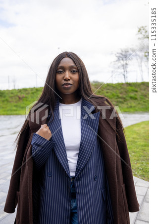 Woman looking stylish in an overcoat and blazer, posing outdoors with confidence and elegance 115335185