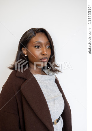 A stylish young woman exudes confidence while standing against a white wall in an elegant outfit A stylish young woman exudes confidence while standing against a white wall in an elegant outfit 115335194