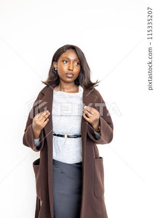 Confident woman in professional attire wears a brown coat with a serious expression, at work Confident woman in professional attire wears a brown coat with a serious expression, at work 115335207