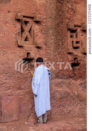 Man in white cloak praying at the walls of rock hewn monolithic ortodox church of Bete Maryam, Lalibela, Amhara Region, Ethiopia. 115335408