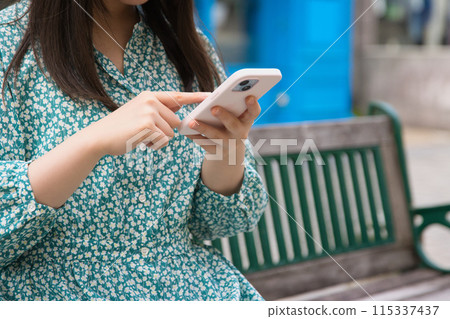 A young woman operating a smartphone on a street corner 115337437