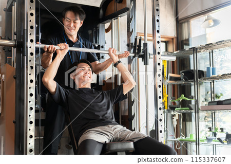 一名男子在健身房接受個人訓練，一名男子擔任訓練師/教練 115337607
