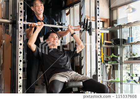 一名男子在健身房接受個人訓練，一名男子擔任訓練師/教練 115337608