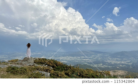 on the highest mountain in Portugal stands a girl her hair blows in the wind standing on top of the mountain relaxing and enjoying beautiful summer mountain landscape. A panoramic view  115342804