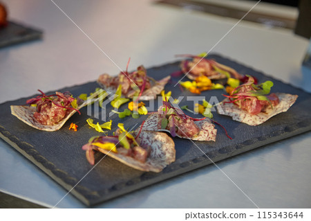 Appetizers on a slate plate with edible flowers and herbs offer a sophisticated dining experience Appetizers on a slate plate with edible flowers and herbs offer a sophisticated dining experience 115343644