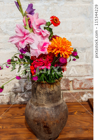 Bouquet of flowers in antique rustic clay jug against white brick wall Bouquet of flowers in antique rustic clay jug against white brick wall 115344229