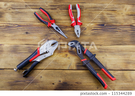 Set of different pliers on wooden background. Top view Set of different pliers on wooden background. Top view 115344289
