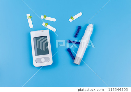 Digital glucometer, lancet pen, disposable needles and test strips on pastel blue background. Top view. Diabetes concept 115344303