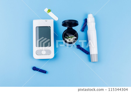 Digital glucometer, lancet pen, disposable needles and test strips on pastel blue background. Top view. Diabetes concept 115344304