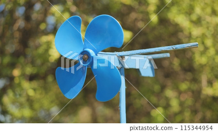 A blue vane weathervane spins in the wind in the summer. 115344954
