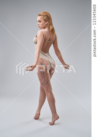 Graceful woman in bodysuit standing back in studio 115345608