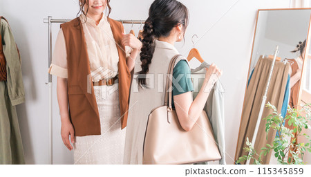 一位女顧客在服飾店照鏡子,要求女店員搭配她的服裝。 一位女顧客在服飾店照鏡子,要求女店員搭配她的服裝。 115345859
