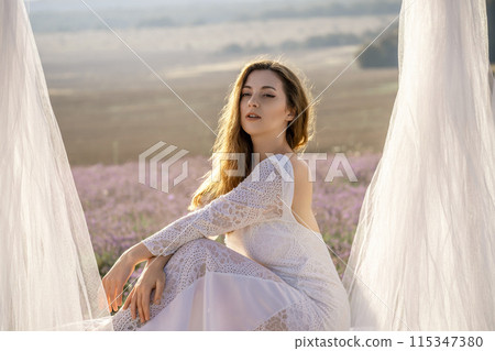A woman in a white dress sits in a field with a white canopy above her. The scene is serene and peaceful, with the woman looking out over the landscape. A woman in a white dress sits in a field with a white canopy above her. The scene is serene and peaceful, with the woman looking out over the landscape. 115347380