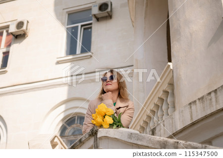 A woman wearing sunglasses and holding a bouquet of yellow flowers stands on a balcony. The scene is peaceful and serene, with the woman looking out over the city. A woman wearing sunglasses and holding a bouquet of yellow flowers stands on a balcony. The scene is peaceful and serene, with the woman looking out over the city. 115347500