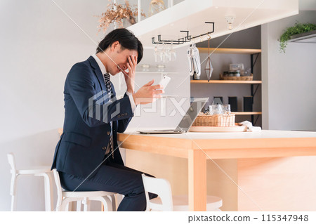 一位亞洲商人在看著他的智慧型手機時感到沮喪/失望（智慧型手機詐欺、網路詐欺、震驚、失敗） 115347948
