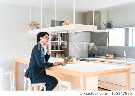 A young male businessman in a suit working on a laptop at a dining table before going to work 115347950