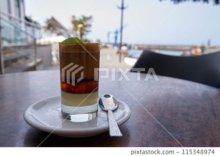 A Barraquito, canarian coffee on a table next to the sea. A Barraquito, canarian coffee on a table next to the sea. 115348974