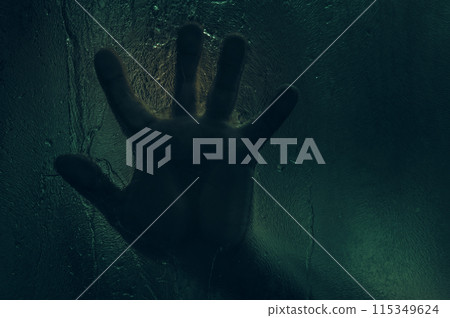 Horror scene of a man against wet glass. Hand against the background of a wet glass bathroom wall. Toned image. 115349624