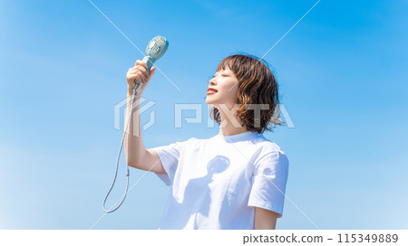 A woman in a white T-shirt cools off with a handheld fan - heat stroke prevention 115349889