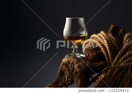 Brandy snifter and rope on a old wooden snag. 115350472
