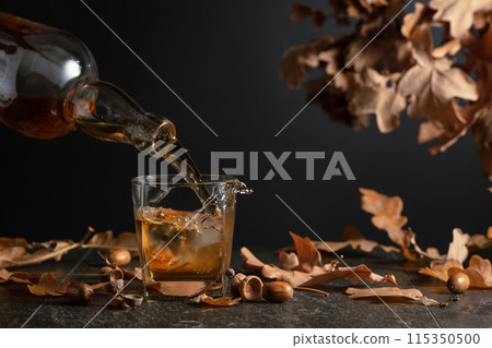 Whiskey with ice on a black table with dried-up oak leaves. Whiskey with ice on a black table with dried-up oak leaves. 115350500
