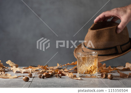 Whiskey with ice on a stone table with dried oak leaves. 115350504