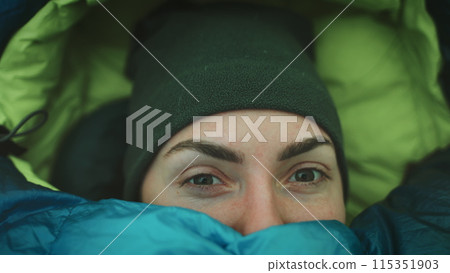 Person wake up in camp tent sleeping bag. Close up portrait of tourist girl opening eyes in cold morning. Female travel wilderness vacation, tourism and camping in outdoor trip. Slow motion 4K Person wake up in camp tent sleeping bag. Close up portrait of tourist girl opening eyes in cold morning. Female travel wilderness vacation, tourism and camping in outdoor trip. Slow motion 4K 115351903
