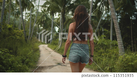 A woman walks down a dirt road surrounded by lush palm trees on Koh Phangan Island, Thailand. A woman walks down a dirt road surrounded by lush palm trees on Koh Phangan Island, Thailand. 115351935