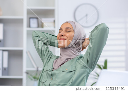Woman in hijab stretching and relaxing at office workspace with a blissful expression. Concept of work-life balance, well-being, and relaxation 115353491