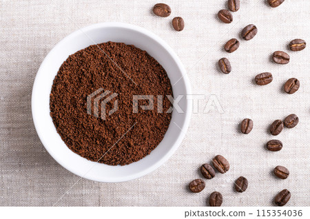 Coffee powder, freshly ground coffee beans in a white bowl on linen fabric. On the right roasted seeds of berries from Coffea arabica, also Arabian, mountain or arabica coffee. Close-up, from above. Coffee powder, freshly ground coffee beans in a white bowl on linen fabric. On the right roasted seeds of berries from Coffea arabica, also Arabian, mountain or arabica coffee. Close-up, from above. 115354036