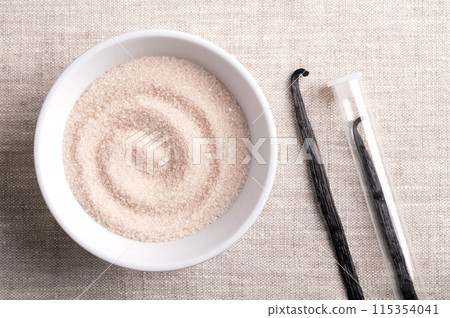 Vanilla sugar, flavored sugar in a white bowl on linen fabric, next to dried, brown, ripe pods or beans of Vanilla planifolia, a spice with distinctive flavor, used for baking and food flavoring. Vanilla sugar, flavored sugar in a white bowl on linen fabric, next to dried, brown, ripe pods or beans of Vanilla planifolia, a spice with distinctive flavor, used for baking and food flavoring. 115354041