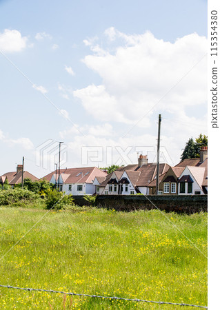 倫敦郊區一排三角形屋頂的房屋和一片黃色花田,在明亮的陽光下,白雲漂浮在倫敦郊區 倫敦郊區一排三角形屋頂的房屋和一片黃色花田,在明亮的陽光下,白雲漂浮在倫敦郊區 115354380