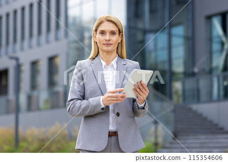 Professional businesswoman in a suit using a tablet outside a contemporary office building, showcasing confidence and modern business technology. Professional businesswoman in a suit using a tablet outside a contemporary office building, showcasing confidence and modern business technology. 115354606