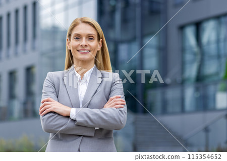 Portrait of a confident business woman in a gray suit standing outdoors with arms crossed in front of a modern office building. Portrait of a confident business woman in a gray suit standing outdoors with arms crossed in front of a modern office building. 115354652