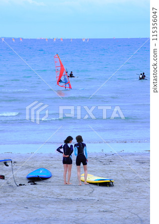 Kids playing in the sea Two girls wearing wetsuits looking at the sea on the beach 115356047