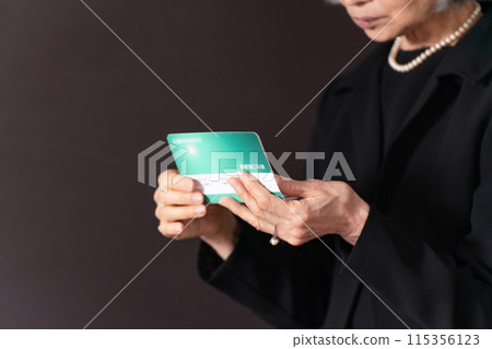 一位身著喪服的老婦人看著她的存摺,哀悼不已。 一位身著喪服的老婦人看著她的存摺,哀悼不已。 115356123