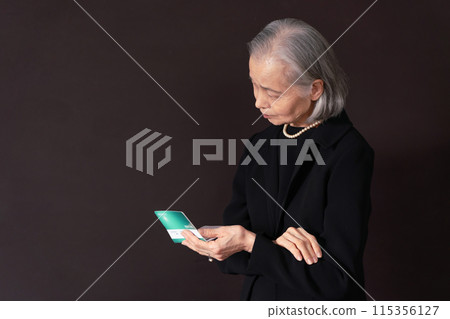 Senior woman in mourning clothes laments as she looks at her bankbook Senior woman in mourning clothes laments as she looks at her bankbook 115356127